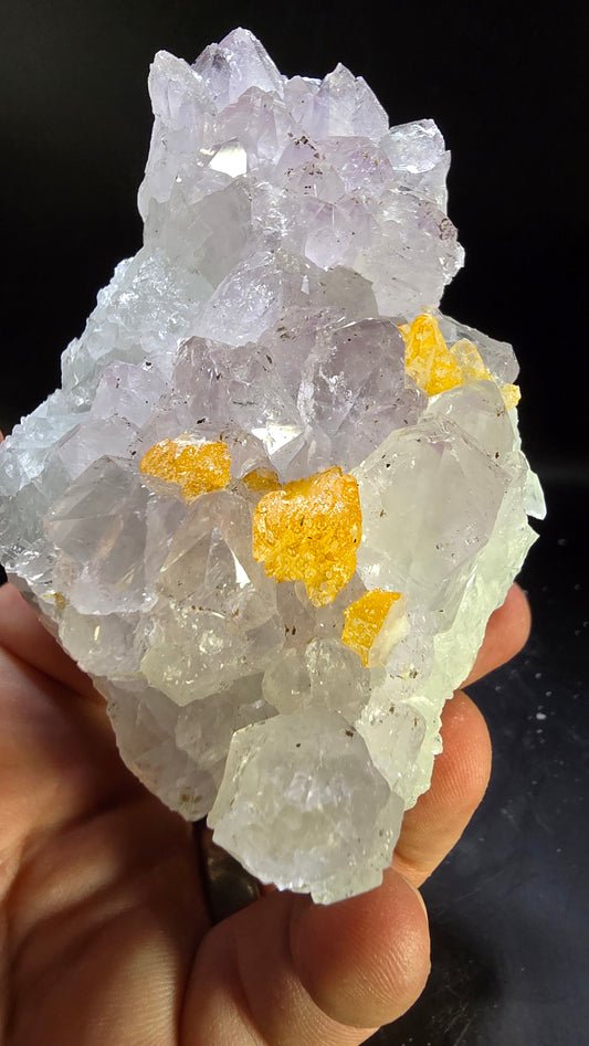 Crystal with yellow inclusions held in a hand against a dark background