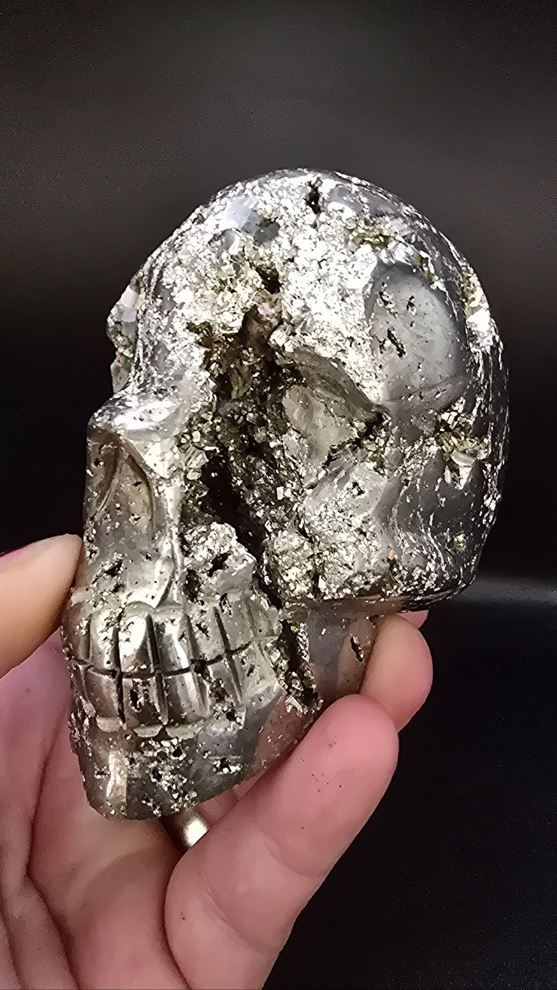 Hand holding a metallic crystal skull against a dark background