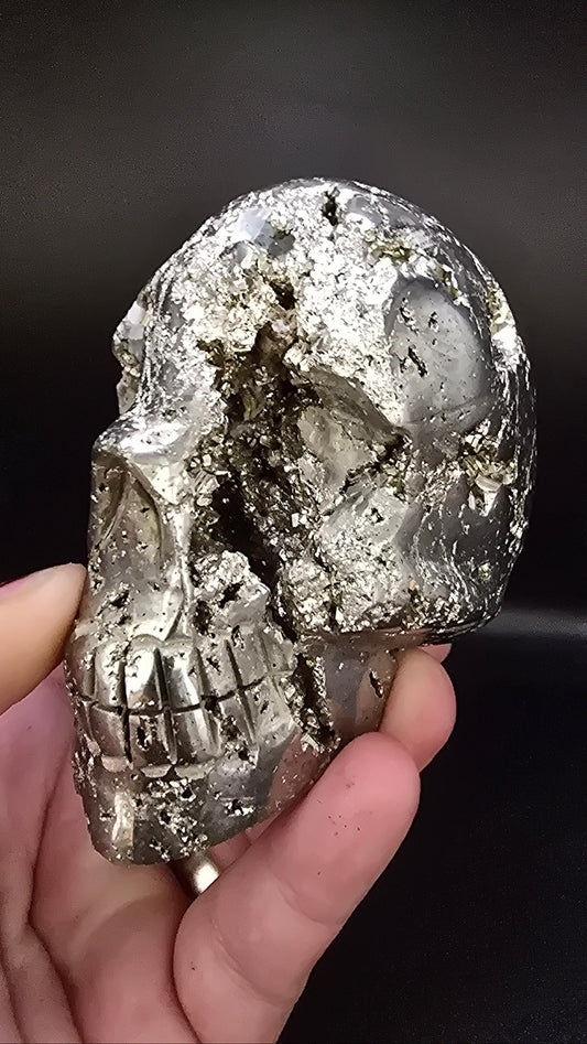 Hand holding a metallic crystal skull against a dark background